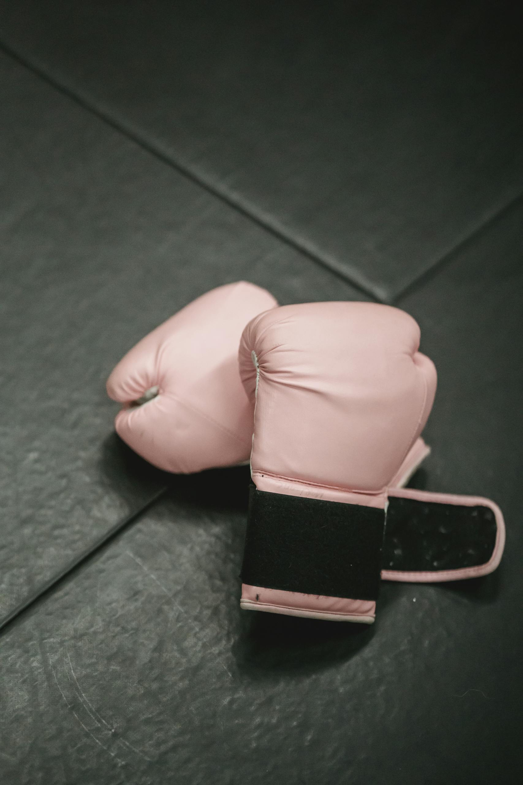 Overhead shot of pink boxing gloves on black gym mat. Ideal for fitness and sports concepts.