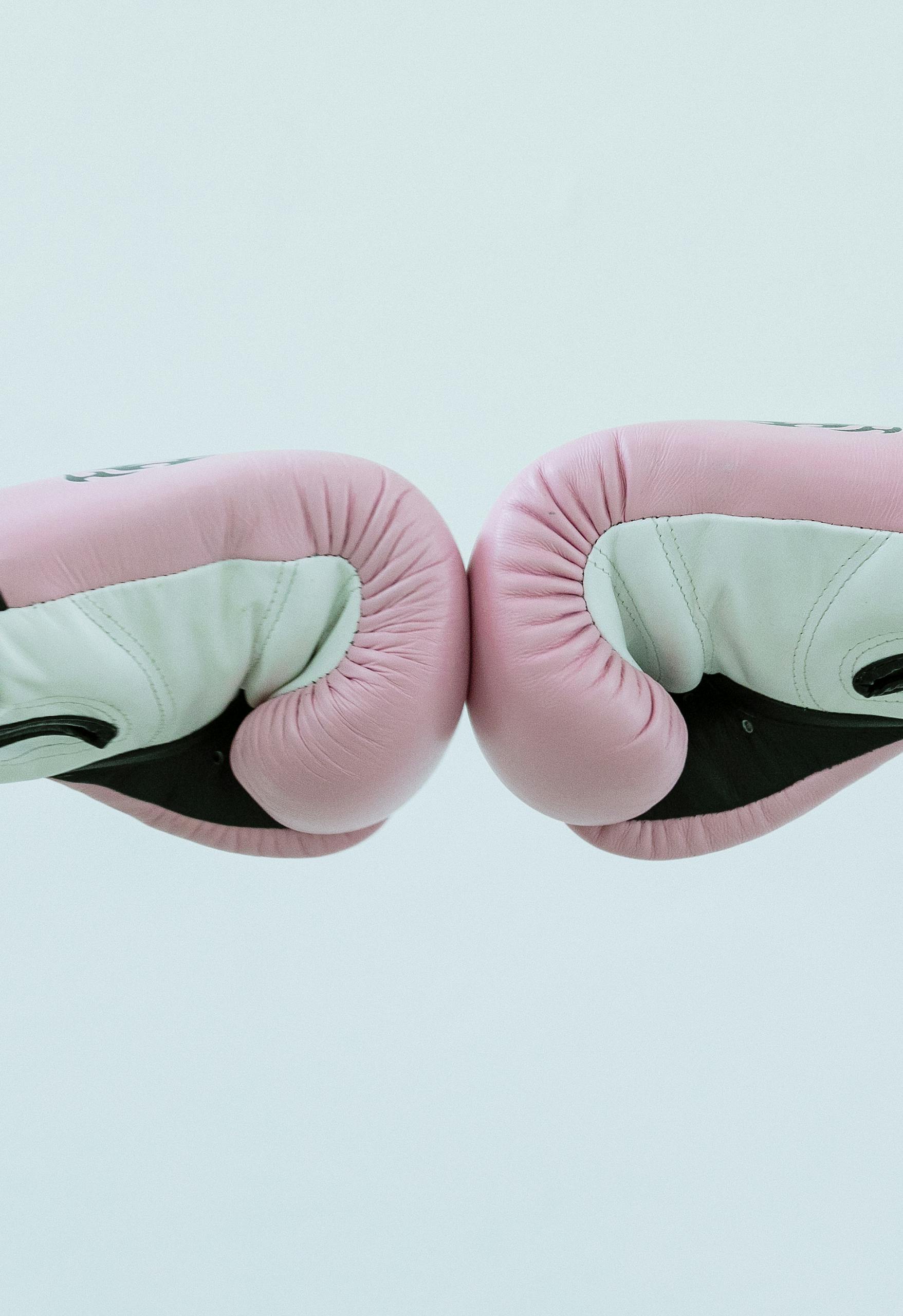 Side view of crop faceless people in pink boxing gloves giving fist bump in bright studio on white background