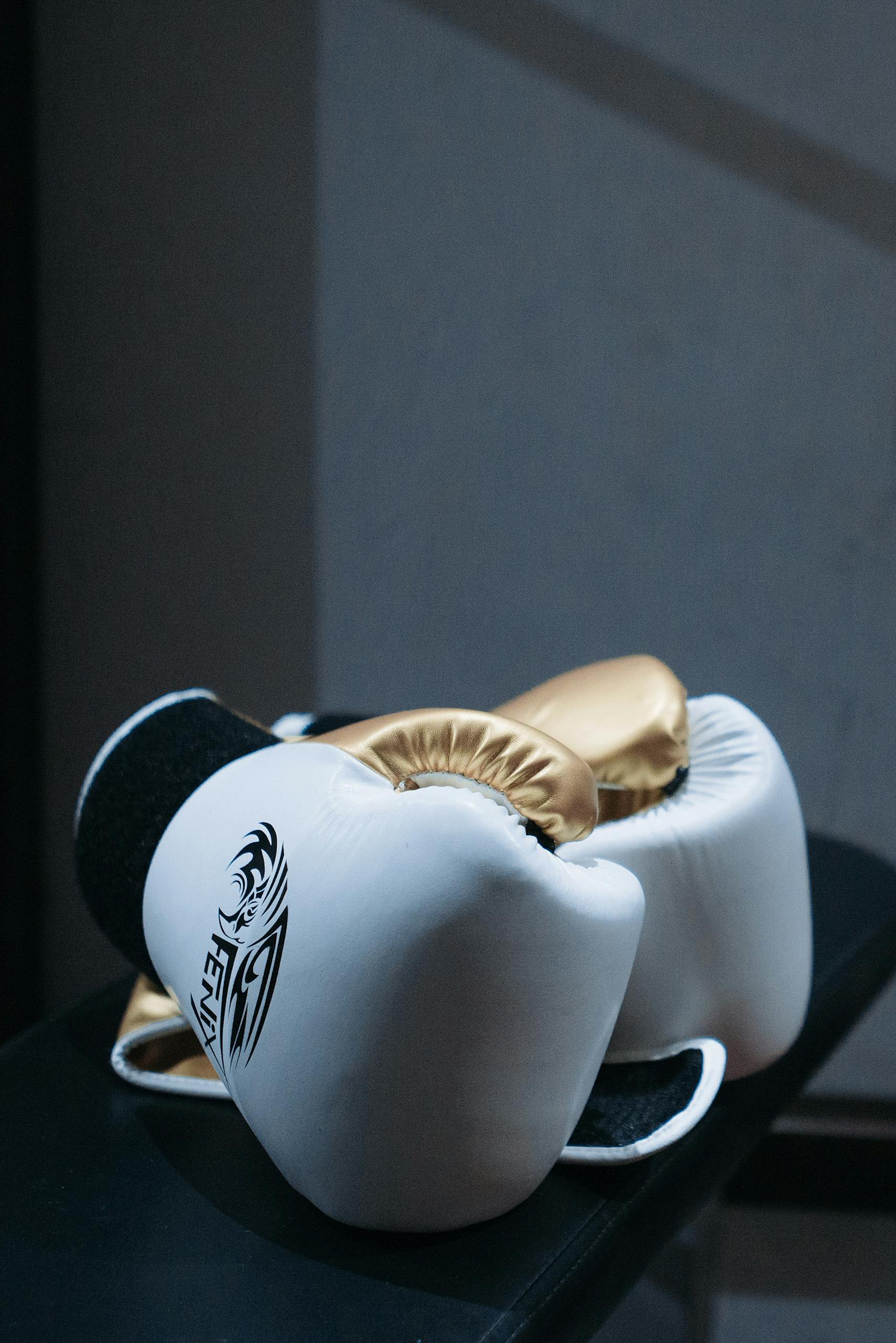 White and gold boxing gloves resting elegantly on a black surface, highlighting their premium quality.
